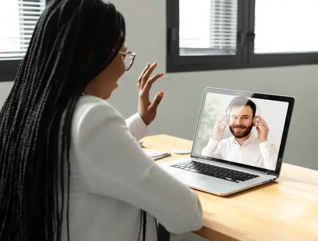 Woman on a laptop in a virtual therapy session with a bearded man on screen.