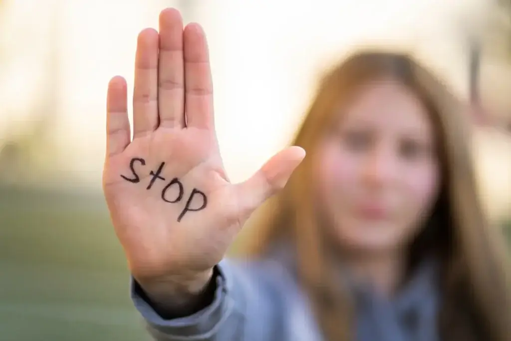Young woman showing her palm with “stop” written on it, symbolizing ending people pleasing.