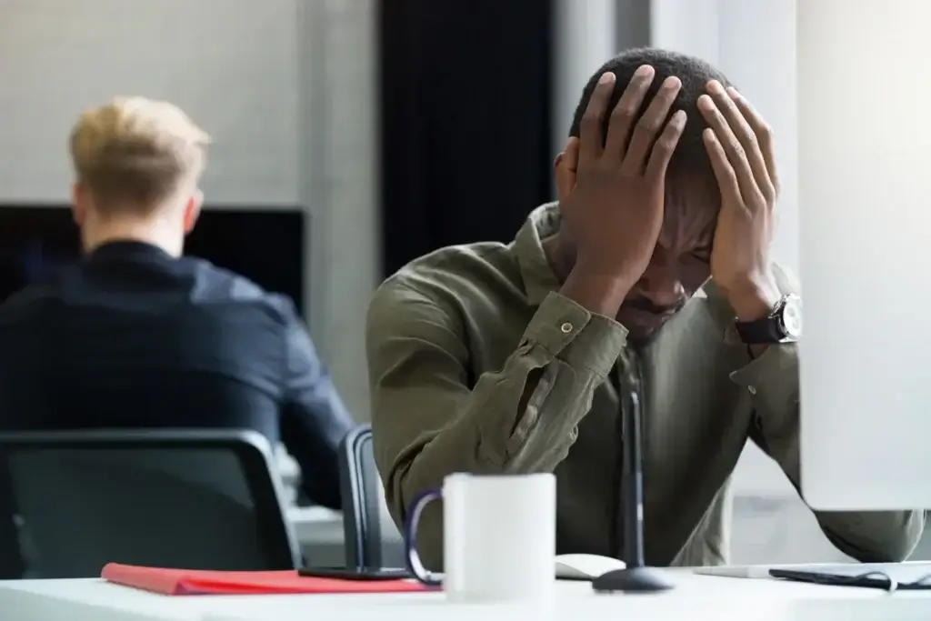 Stressed man sitting at desk, overwhelmed by job-related anxiety.