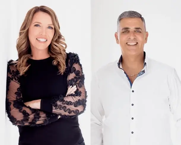 Two professional therapists, a smiling woman in a black top with sheer sleeves and a smiling man in a white shirt, standing side by side against a white background.